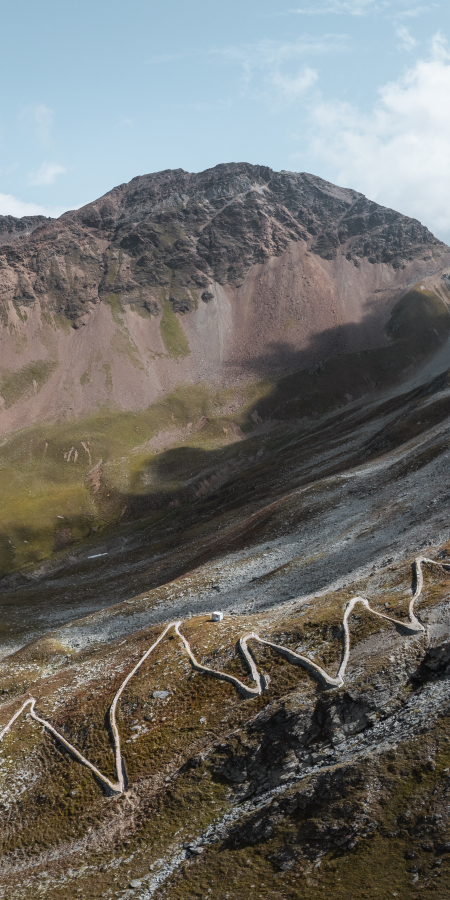 Hochalpine Serpentinenstraße mit mehreren Kehren vor felsigem Bergmassiv.