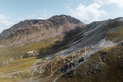Hochalpine Serpentinenstraße mit mehreren Kehren vor felsigem Bergmassiv.