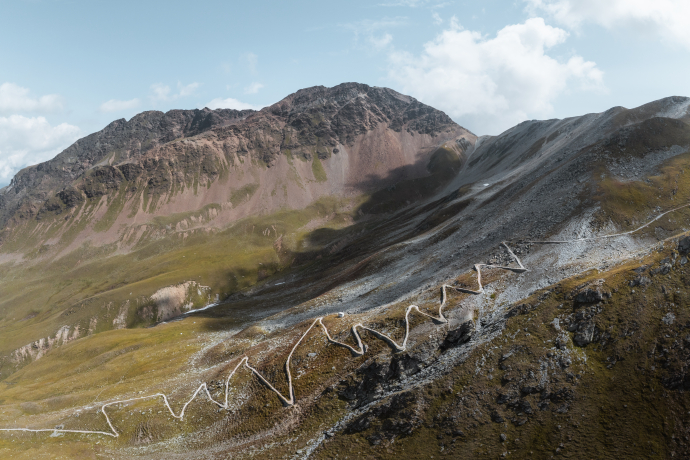 Hochalpine Serpentinenstraße mit mehreren Kehren vor felsigem Bergmassiv.